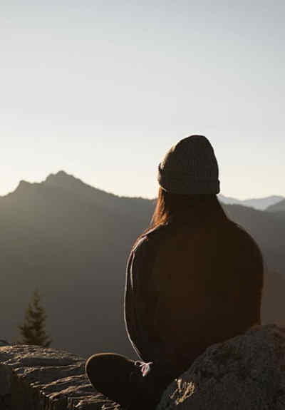 Une dame regarde le soleil se lever derrière des montagnes.