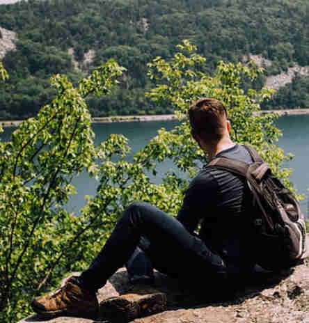 Un jeune homme est assis seul sur une falaise rocheuse surplombant un lac de montagnes