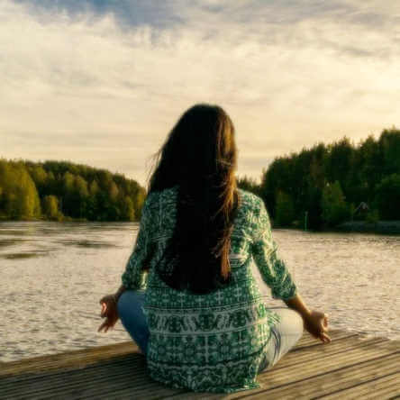 Une femme médite assise devant un lac.