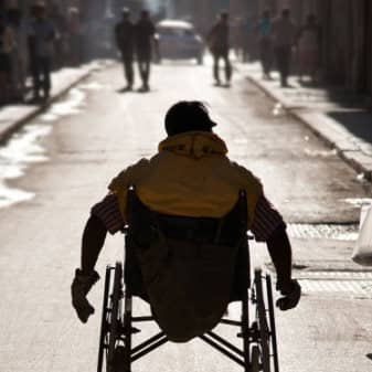  Une personne seule en chaise roulante s'éloigne dans la rue. 