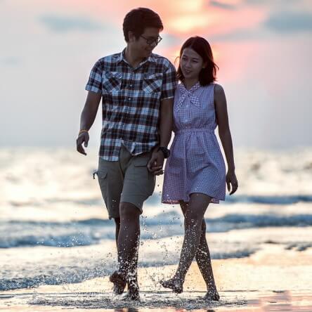 Un jeune homme et une jeune femme main dans la main sur la plage.