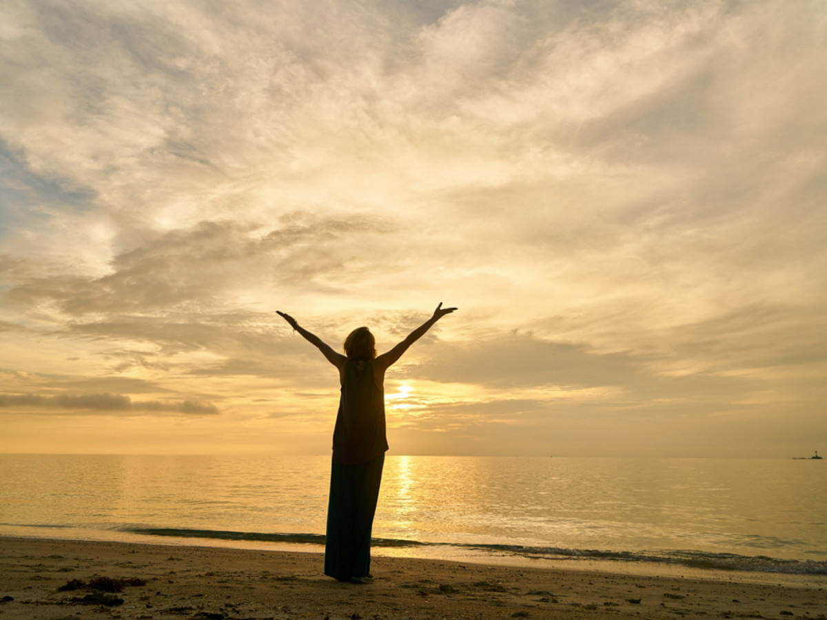 Une dame lève les bras devant un coucher de soleil.