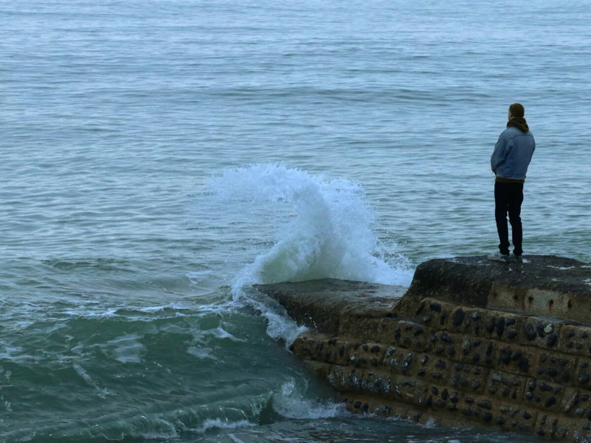 Un homme seul debout face à une mer agitée