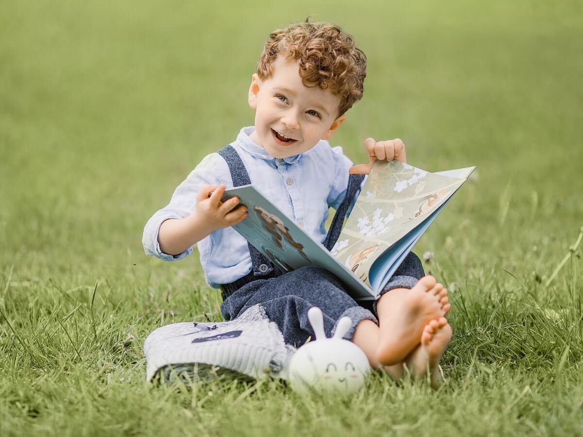 Assis sur du gazon, un gamin ouvre un livre.