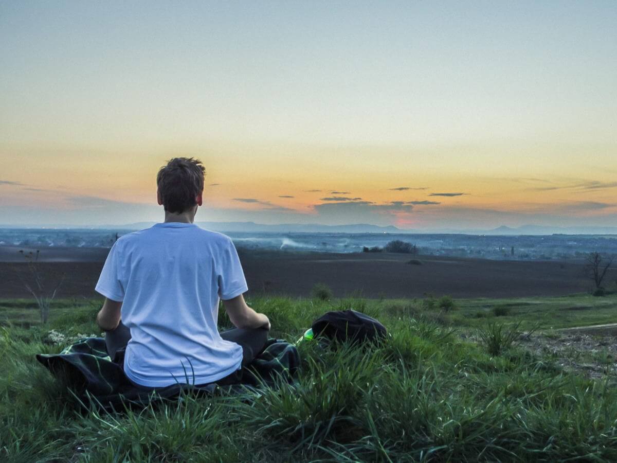 homme est assis en position de Yoga dans un paysage grandiose.