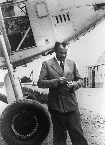 Antoine de Saint-Exupéry prend une cigarette debout devant son avion.