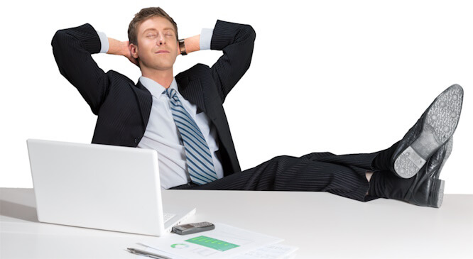 Un jeune homme dort avec les pieds sur son bureau.