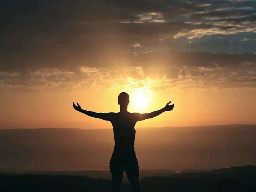 Une personne lève les bras devant la beauté d'un lever de soleil