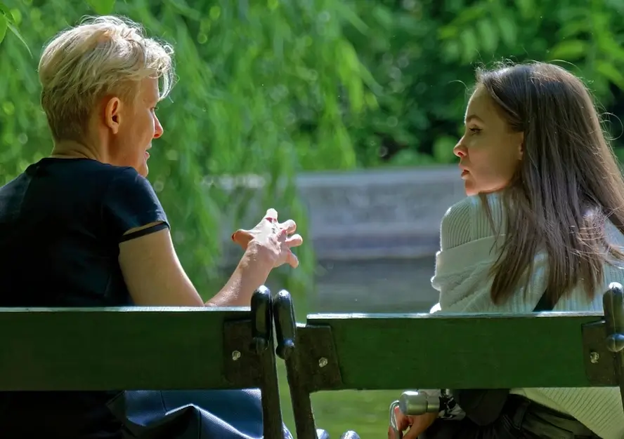 Une homme et une femme discutent assis sur un banc de parc.