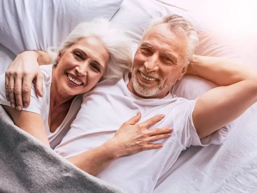 Un couple aux cheveux gris au lit et souriant