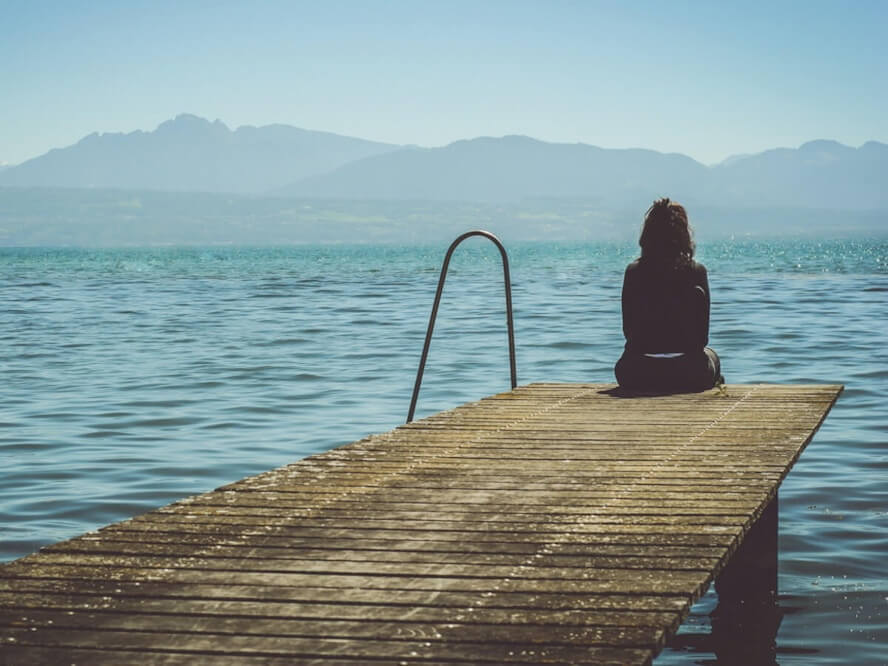 Une dame seule sur un quai près d’un grand lac